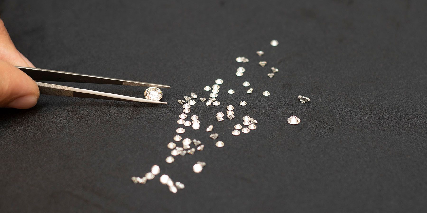 O pensetă ține un diamant deasupra unor diamante libere de mărimi diferite, pe fond negru