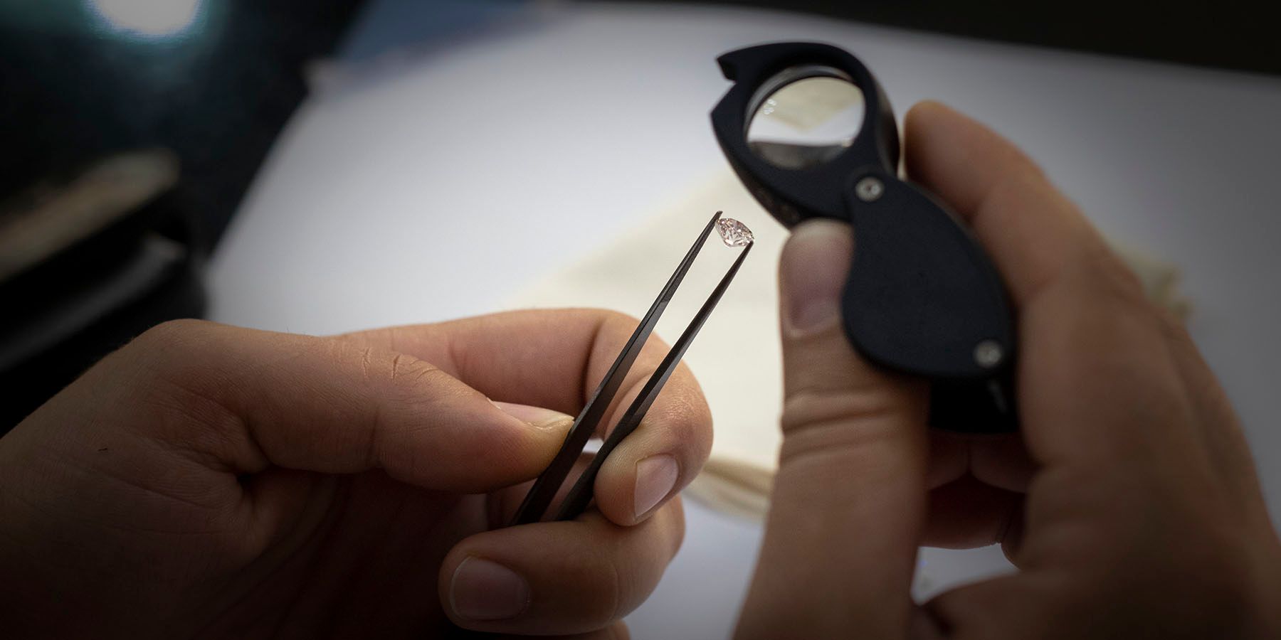 Un evaluator ține un diamant în pensetă și îl examinează cu lupa